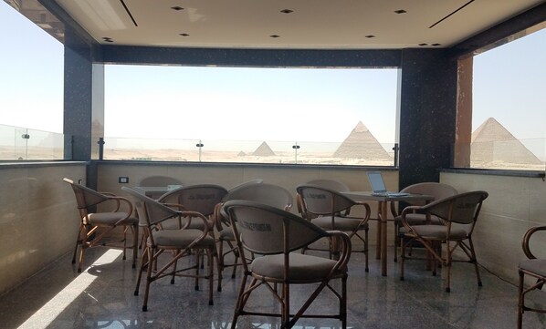 A balcony with wicker chairs and a laptop, overlooking pyramids. - Pyramids Terrace INN (Giza)