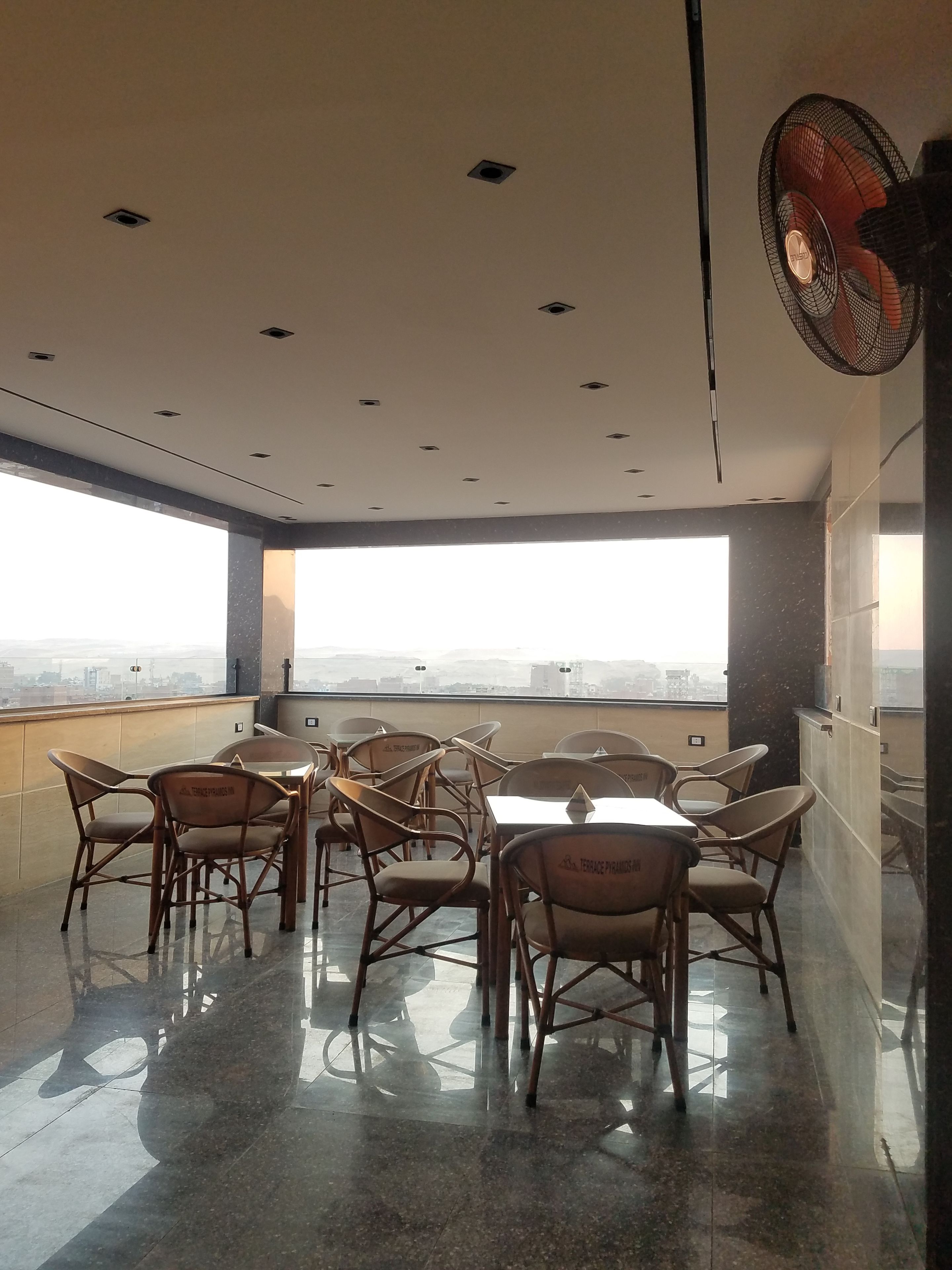 A spacious room with a high ceiling, multiple ceiling lights, a large window offering a city view, and a fan on the wall.