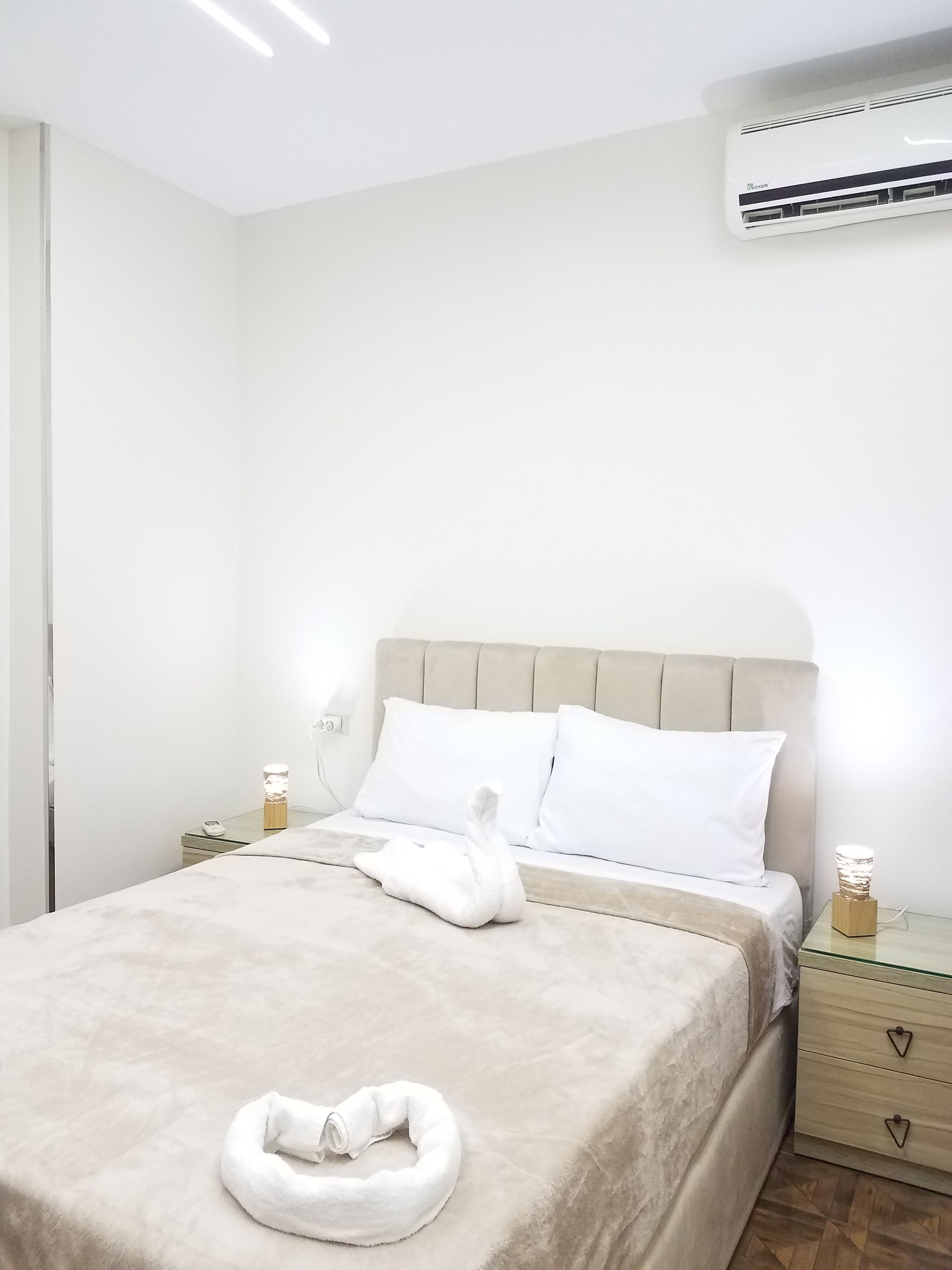 Una habitación de hotel con una cama, una mesita de noche, una lámpara y un aire acondicionado.