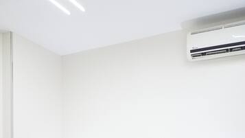 Una habitación de hotel con una cama, una mesita de noche, una lámpara y un aire acondicionado.