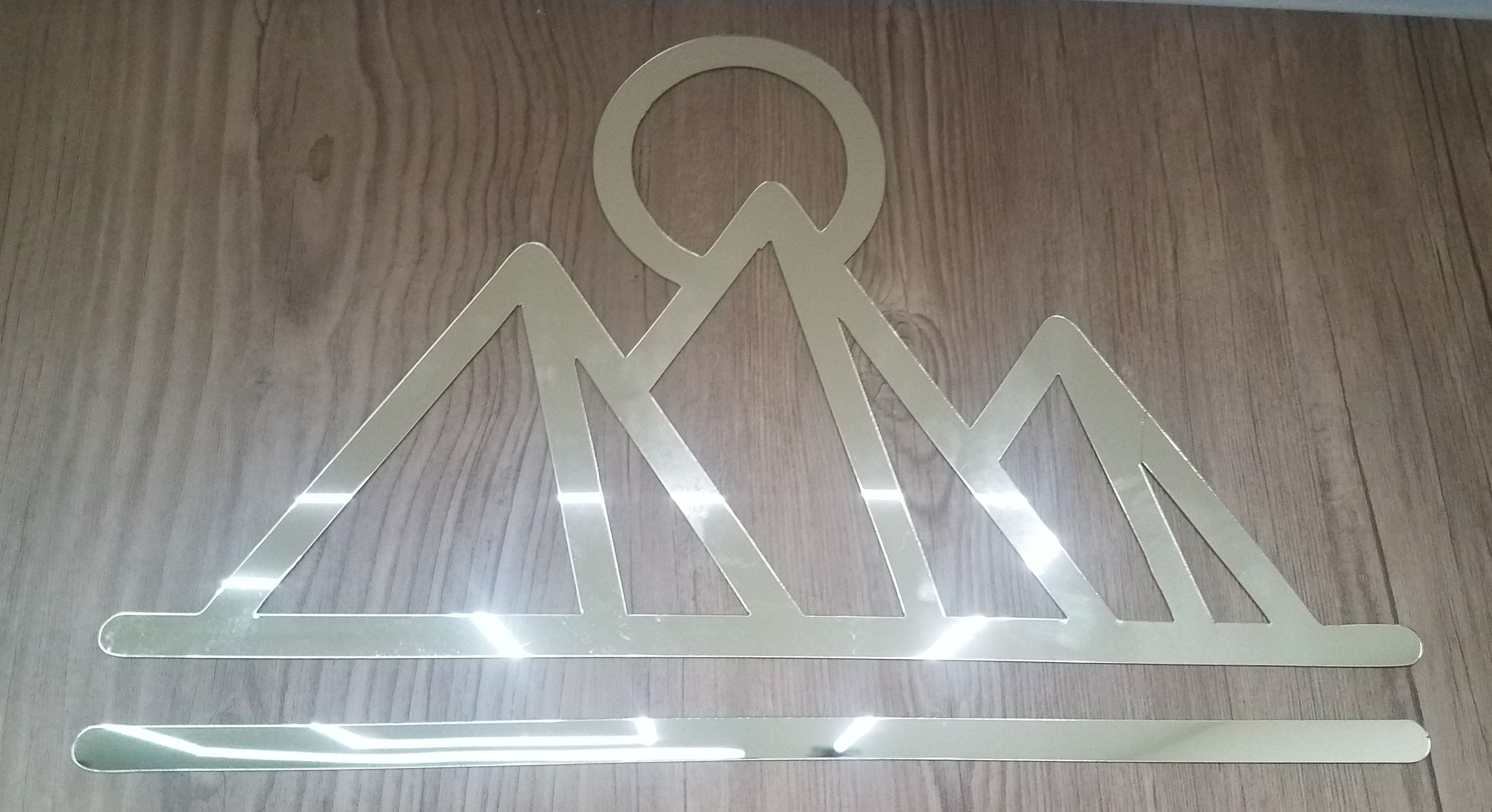 A wooden surface with a metal cut-out design of a mountain range and a circle at the top.
