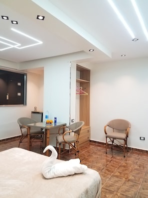 A hotel room with a dining table, two chairs, a bed with a white swan decoration, a wardrobe, and a TV mounted on the wall. - Pyramids Terrace INN (Giza)
