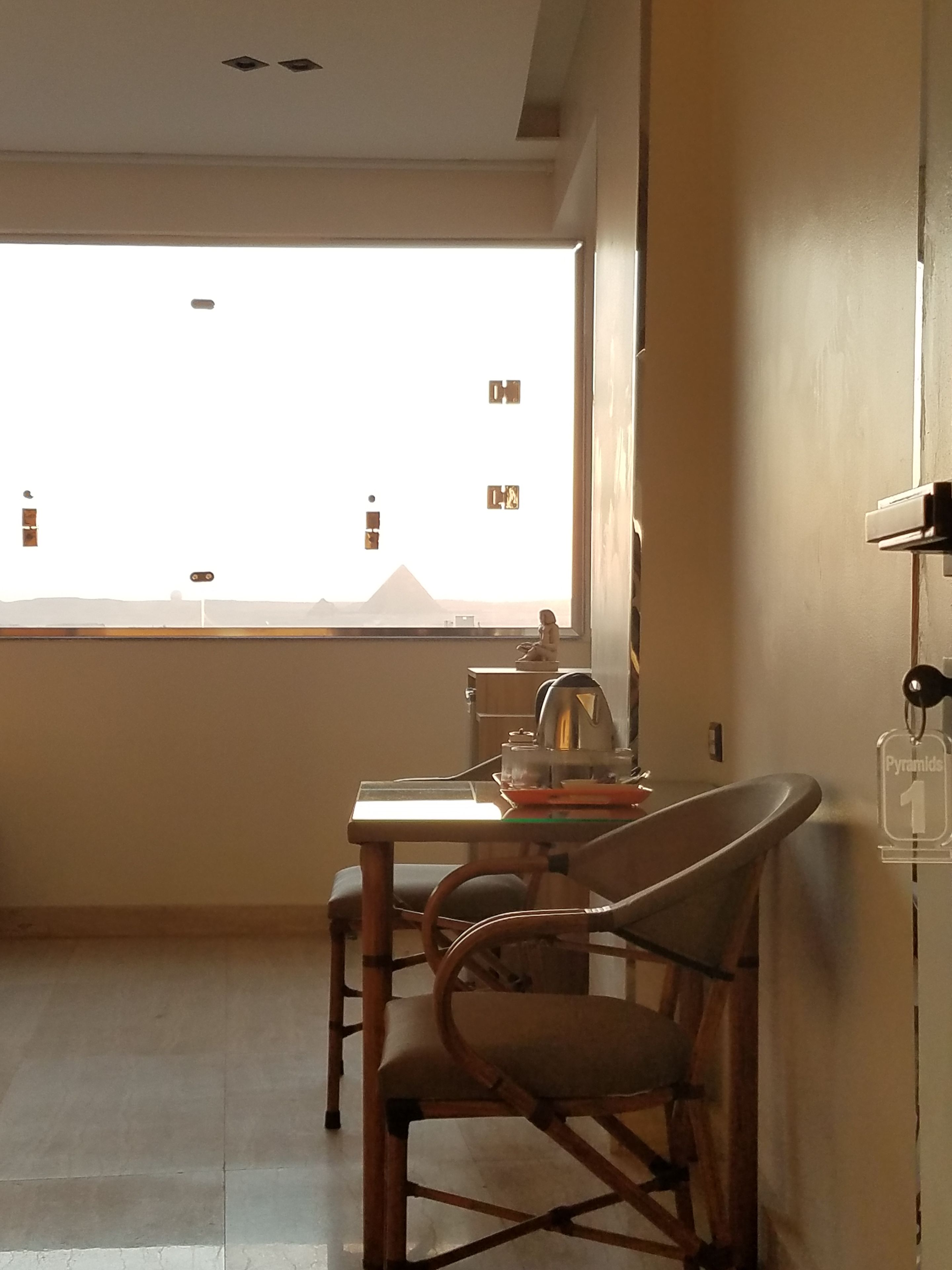 Una habitación con una mesa de comedor, sillas, una ventana con vistas a las pirámides y un estante con un llavero.