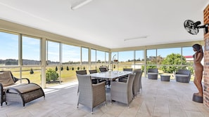Enjoy expansive views of the surrounding landscape from this sunroom with a large dining table and comfortable seating.