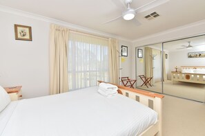 Une chambre à coucher comprenant un lit, une table de chevet, une chaise, un miroir et un ventilateur de plafond.