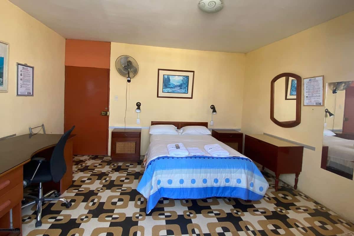 Una habitación de hotel con cama, escritorio, silla y piso estampado.