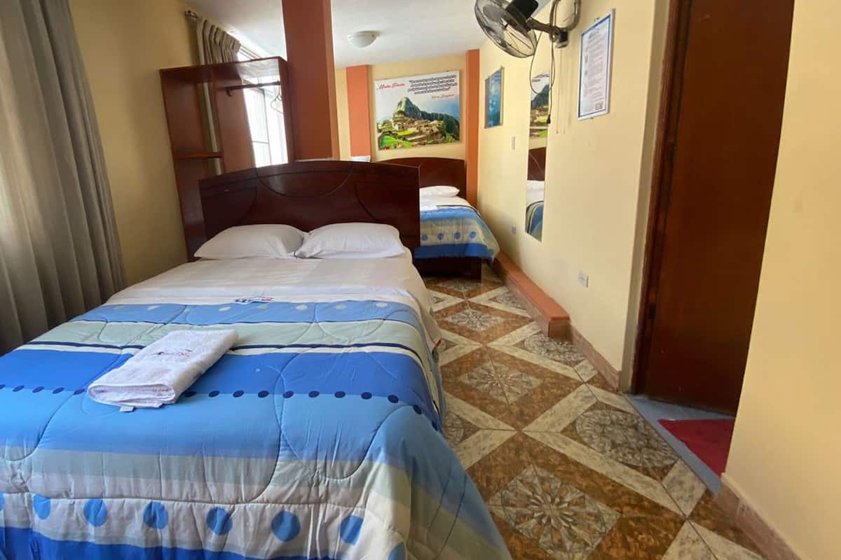 Una habitación de hotel con cama, ventana con cortinas, ventilador de pared y piso de baldosas.