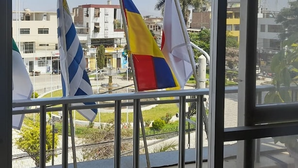 Ein Balkon mit drei Flaggen, Blick auf Gebäude und einem klaren Himmel.