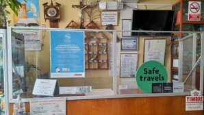 Ein Empfangsschalter mit verschiedenen Schildern und Aushängen, darunter ein Schild mit der Aufschrift 'Safe travels', das Logo 'Hostal Hogar' und ein Schild mit 'Timbre'.
