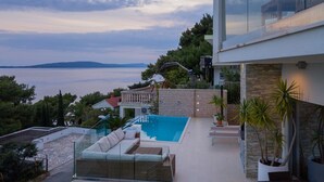 A modern outdoor pool area with a glass balustrade, a seating area, and a view of the sea. - Luxury villa Saga in Drvenik, private pool (Drvenik)