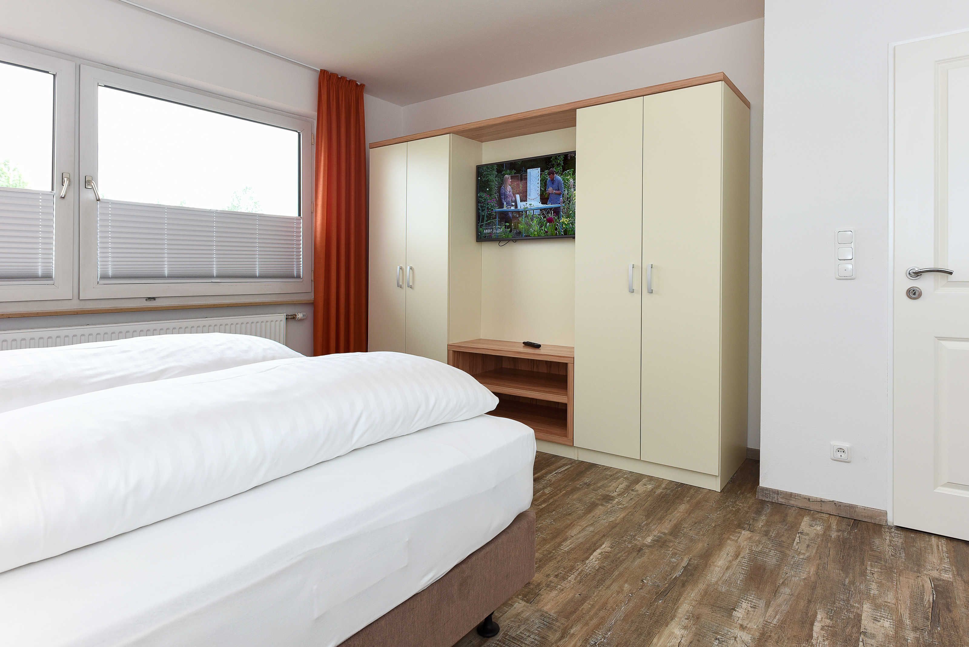 Habitación de hotel con cama, armario, televisión y ventana con persianas.