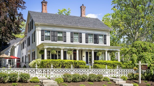 A two-story white colonial-style house with a front porch, columns, and a white picket fence. - Abigail's Inn (Camden)