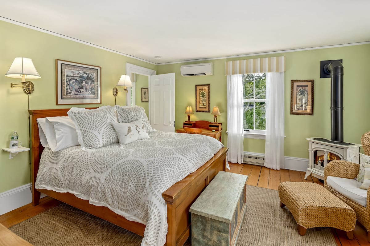 A cozy bedroom with a large bed, bedside tables, a fireplace, and wicker furniture.
