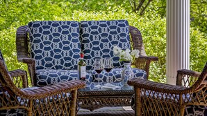 A wicker sofa with a geometric pattern, a glass table with a bottle and glasses, and wicker chairs. - Abigail's Inn (Camden)