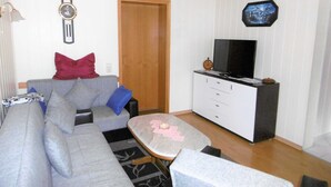 Una sala de estar con un sofá gris, una mesita de centro, un televisor sobre un mueble blanco y un techo de madera.