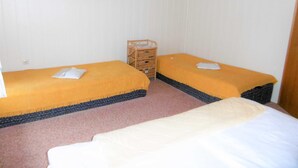 Una habitación con dos camas, un pequeño cofre de madera y tres cuadros colgados en la pared.