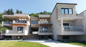A modern multi-story residential building with balconies, a stone facade, and a well-maintained lawn. - Bella Vista Luxury Apartments (Thasos)