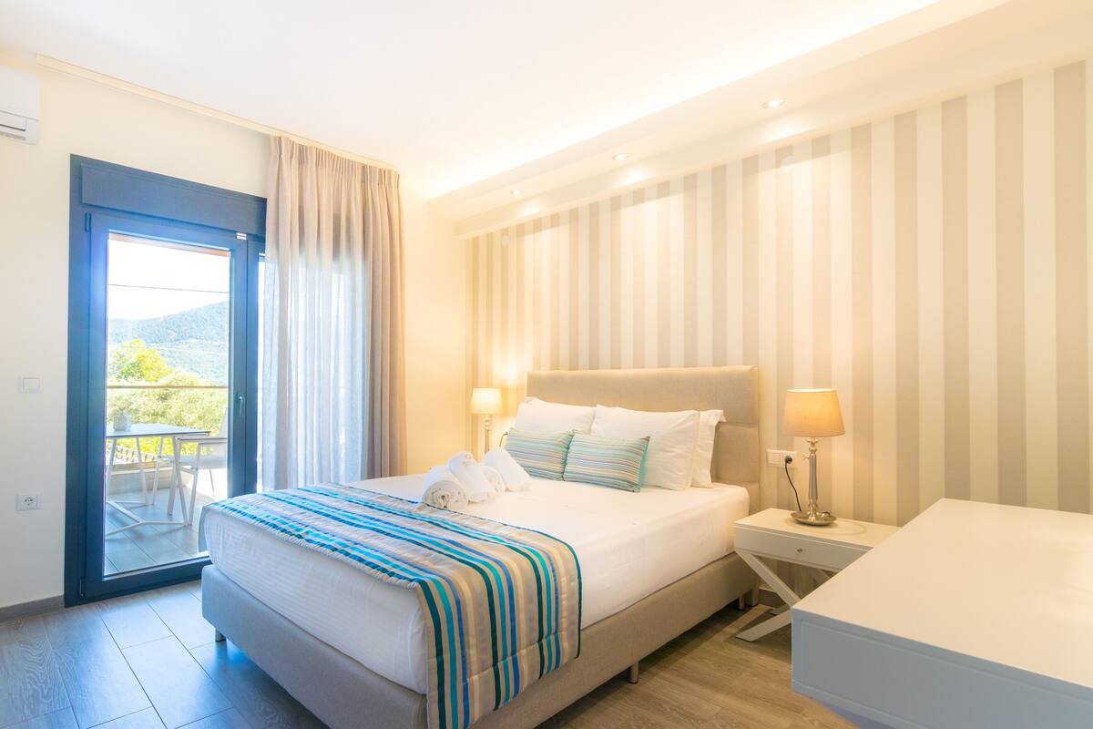 Een hotelkamer met een bed, nachtkastjes, een bureau en uitzicht op het omliggende landschap.