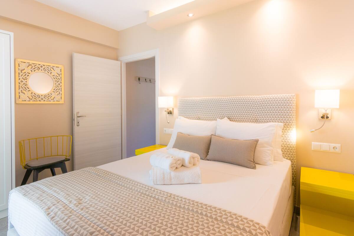 Een net opgemaakt bed met een sprei met geometrisch patroon, een hoofdbord met een getextureerd ontwerp, en twee bedlampen.