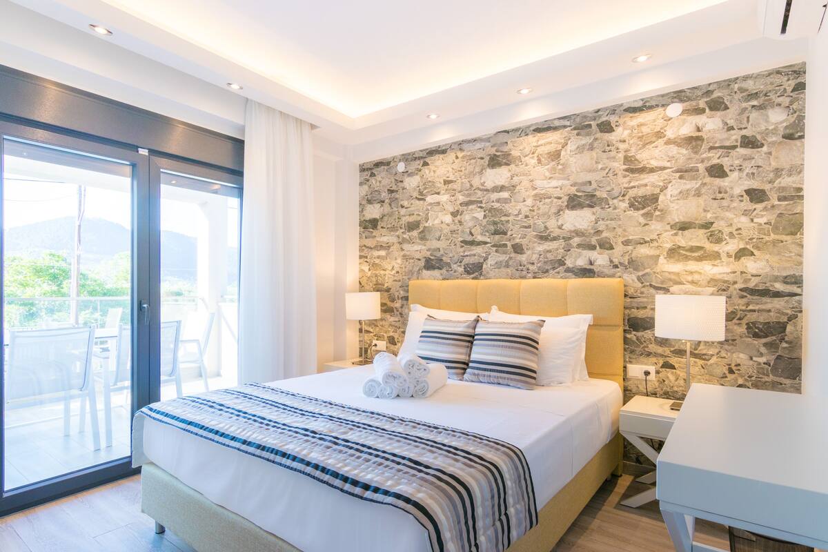 Een moderne hotelkamer met een groot bed, een stenen muur en een balkon met zitplaatsen.