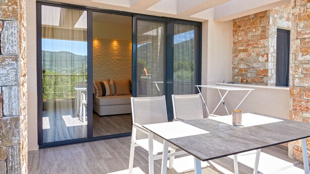 Ein moderner Essbereich im Freien mit Tisch und Stühlen, einer Couch und einer Glastür, die auf einen Balkon mit Landschaftsblick führt.