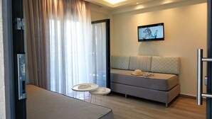 Ein modernes Hotelzimmer mit einer Sitzecke, zwei kleinen Tischen, einem an der Wand montierten Fernseher und einem großen Fenster mit Vorhängen.