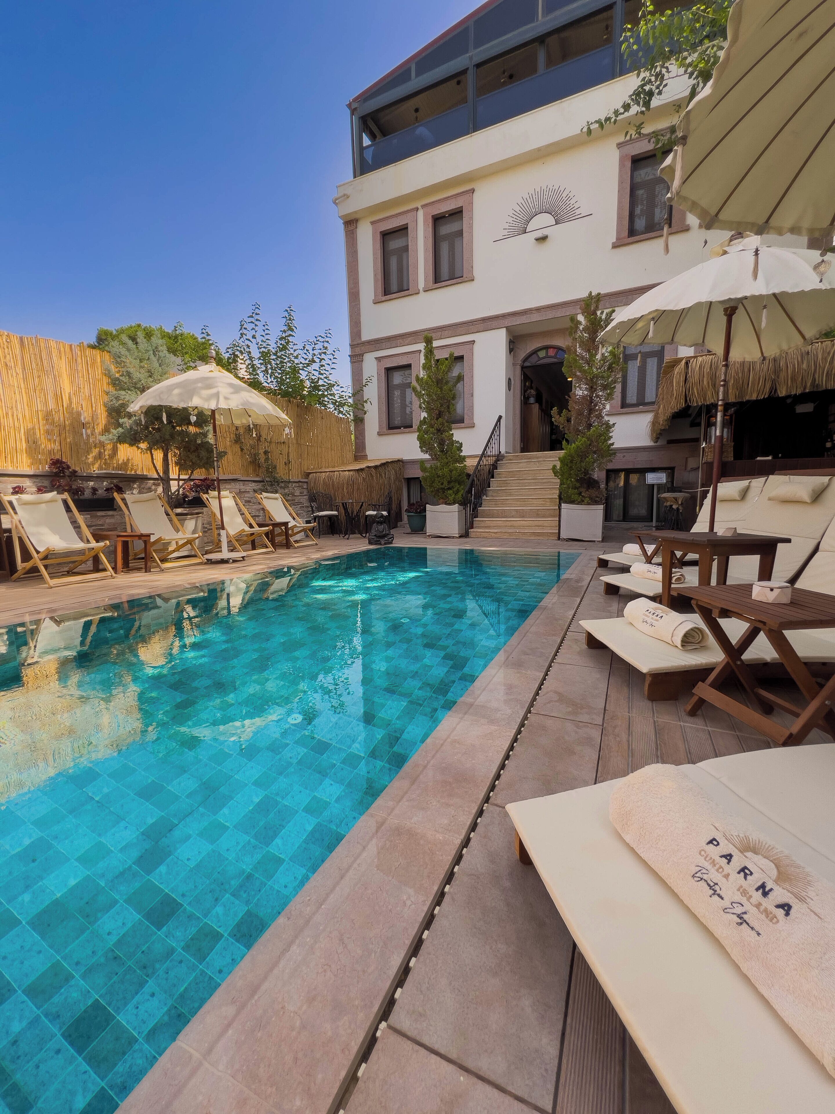 A pool area with lounge chairs and umbrellas, a staircase leading to a building, and a clear blue pool.