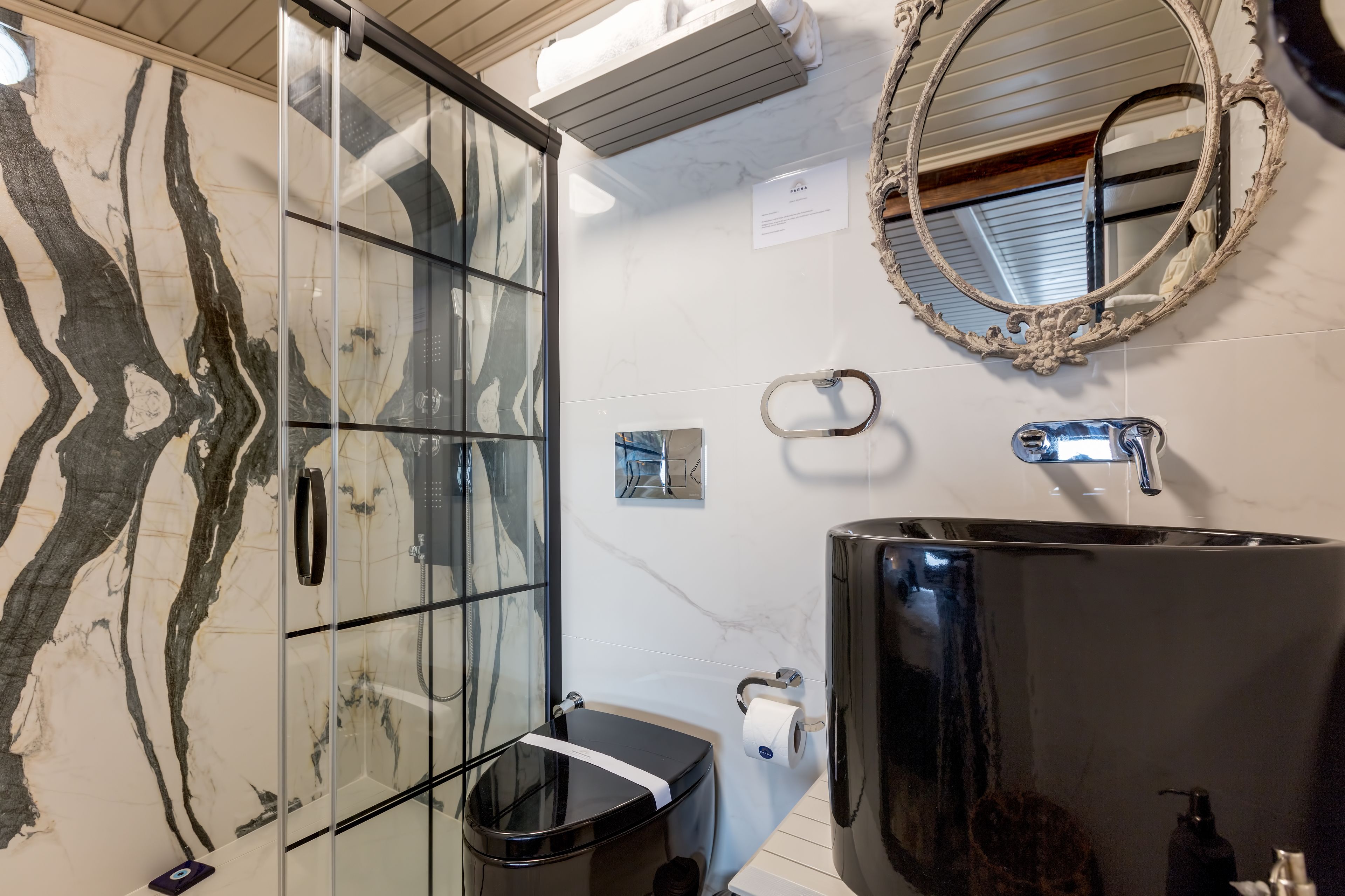 Ein modernes Badezimmer mit Duschkabine aus Glas, Toilette in Schwarz, großem Spiegel und Wandverkleidung aus Marmor.