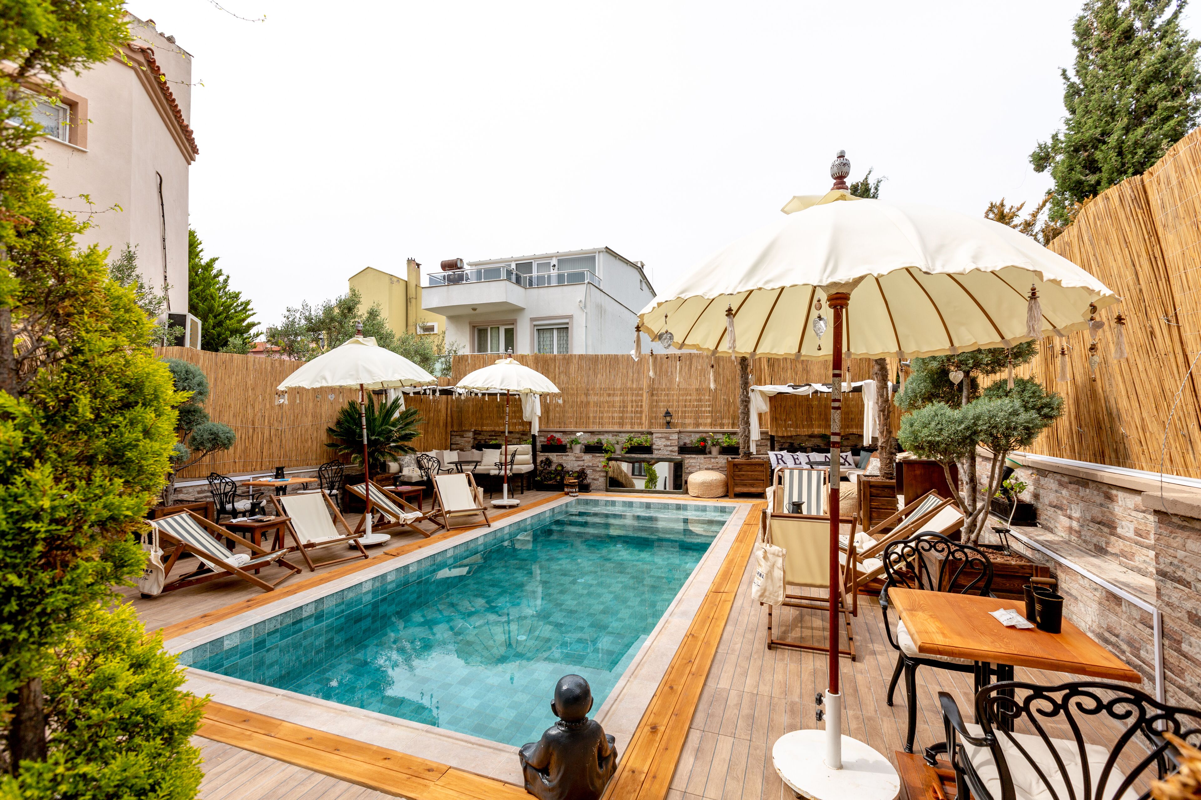 A swimming pool with lounge chairs and umbrellas, surrounded by wooden fencing and greenery.