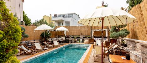 A swimming pool with lounge chairs and umbrellas, surrounded by wooden fencing and greenery.