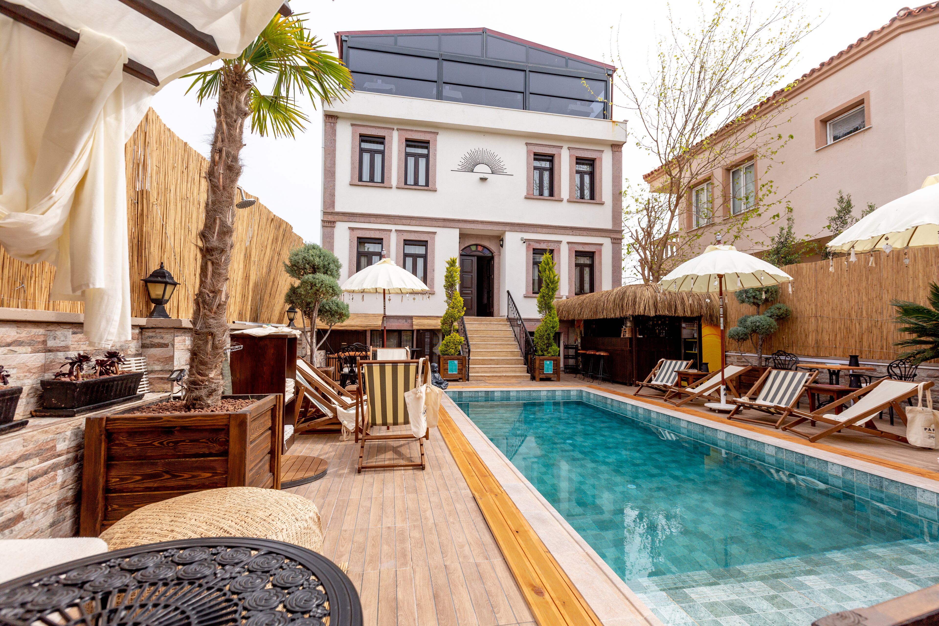 A pool area with lounge chairs, a palm tree, and a building with a balcony.