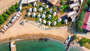 An aerial view of a resort with a beach, clear waters, and a dock with umbrellas. - Parna Hotel (Ayvalik)