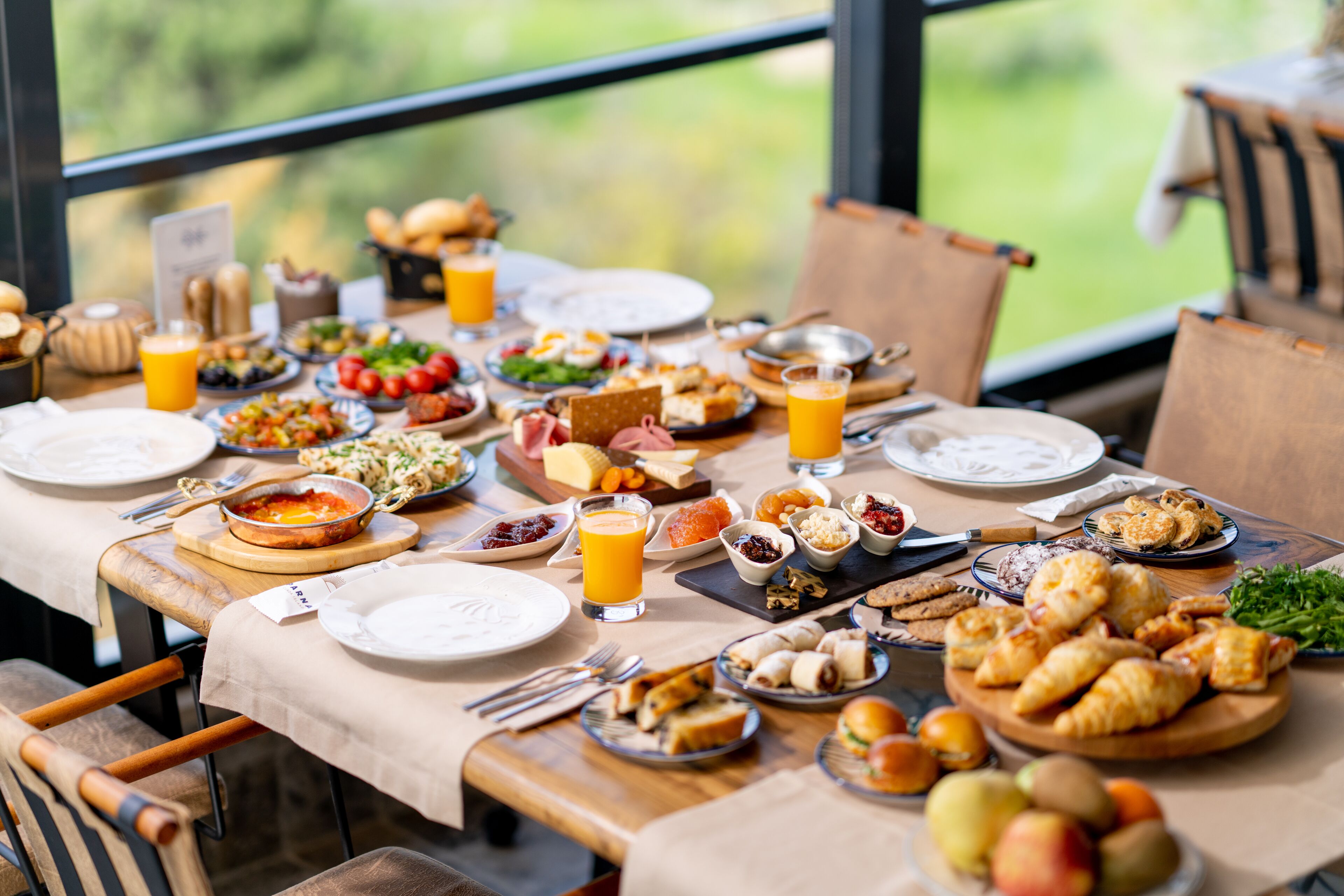 A breakfast buffet with a variety of dishes and drinks, set on a table with a view of greenery outside.