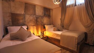 A hotel room with two beds, a decorative headboard, a nightstand with a lamp, and a window with curtains.