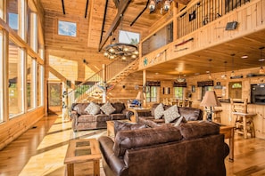 Cozy cabin-style living area with a high ceiling, staircase, and kitchen.