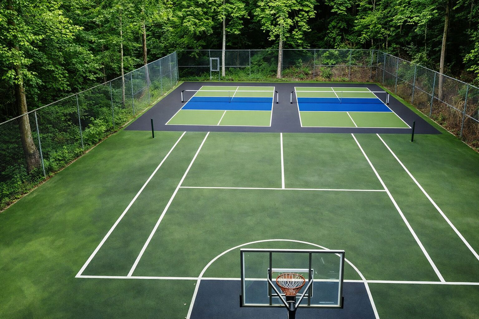 Un court de tennis extérieur comprenant deux terrains, entouré d’une clôture en métal et d’arbres.