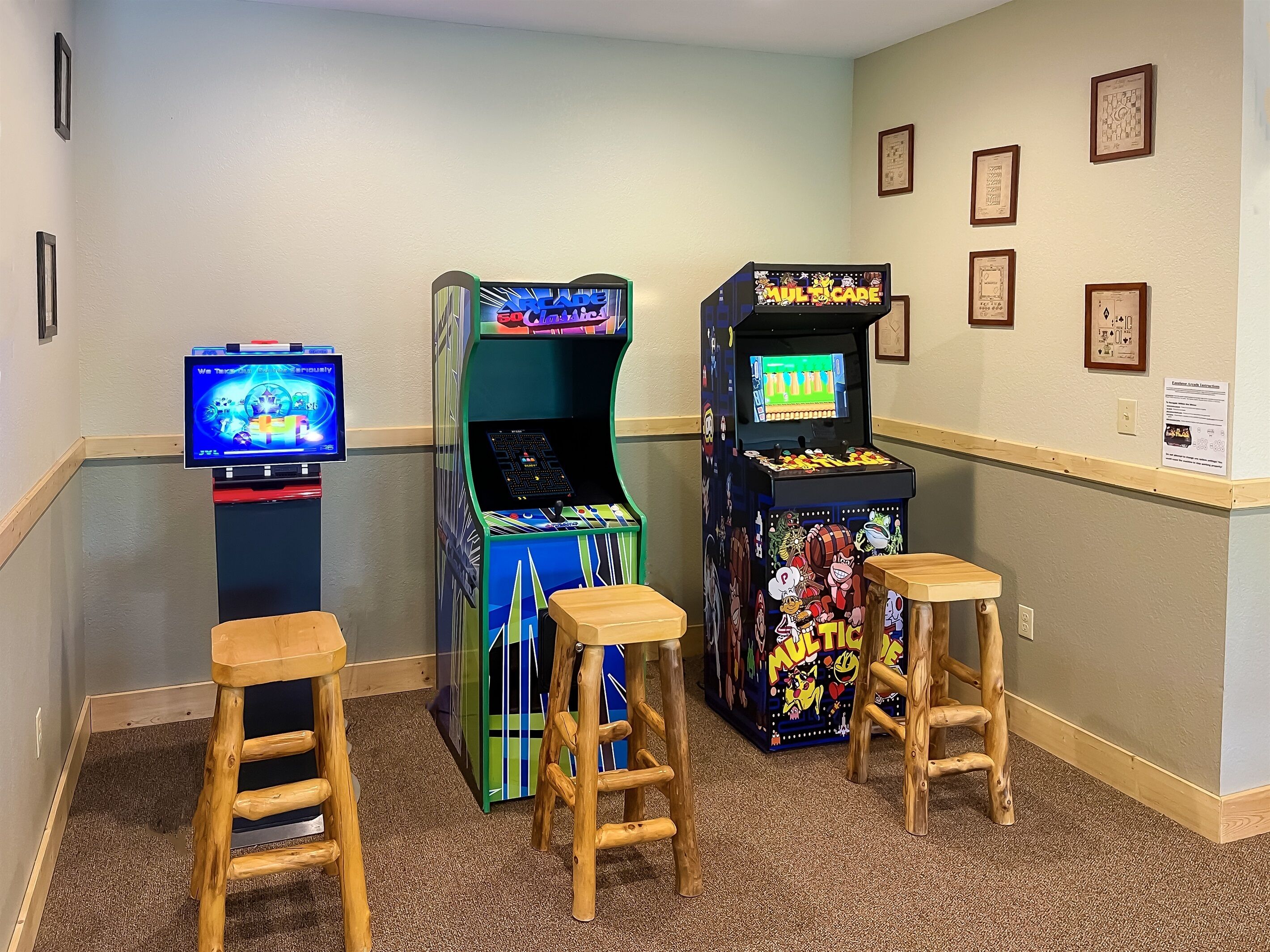 A room with arcade games, wooden stools, and framed pictures on the wall.