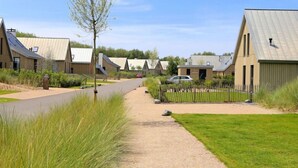 A row of modern, single-story buildings with sloped roofs, a gravel path, and a fenced area with a car parked nearby. - Oesterdam Resort by Interhome (Tholen)