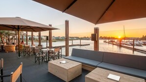 An outdoor seating area with tables and chairs, a wooden bench, and umbrellas providing shade. - Oesterdam Resort by Interhome (Tholen)