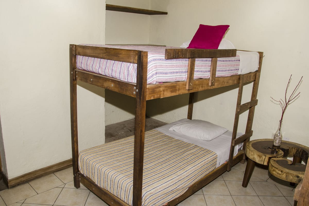 Una cama litera con un colchón a rayas, una almohada blanca y una almohada rosa encima.
