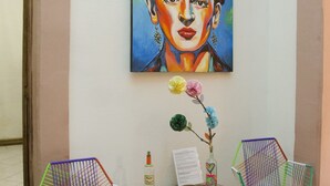 A lobby with two colorful chairs, a wooden table, and a painting of a woman with roses on the wall. - Maria Bonita - Hostel (Guadalajara)