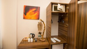 Ein Hotelzimmer mit einem Holztisch, einem Gemälde, einer Zimmerpflanze, einer Mikrowelle und einem Kleiderschrank.