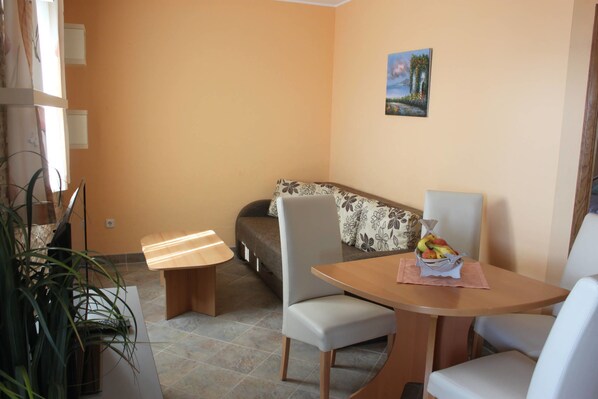 A small, cozy room with a sofa, a dining table with chairs, and a potted plant.