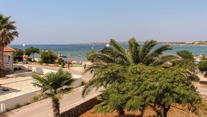 Zona costera con un paseo pavimentado, palmeras y una playa al fondo.