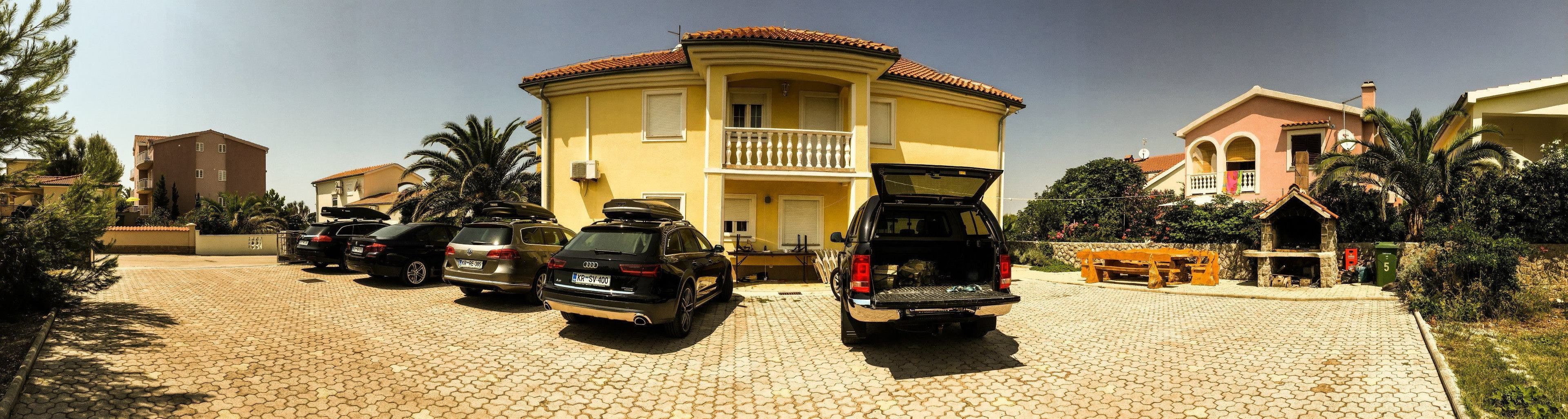 A yellow building with a balcony, parked cars, and a stone fireplace.