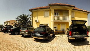 Un edificio amarillo con balcón, coches aparcados y chimenea de piedra.