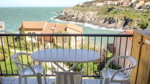A balcony with a table and chairs overlooking a coastal view with houses in the background. - Les Roches Bleues by Interhome (Collioure)