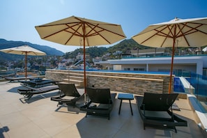 Eine Dachterrasse mit Liegestühlen, Sonnenschirmen und einem Pool mit Blick auf eine Hügelstadt.