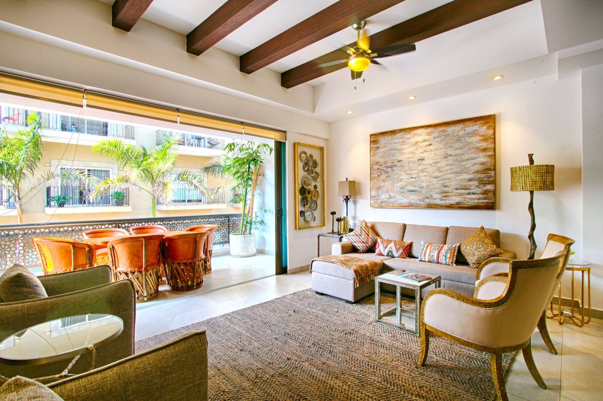 A spacious living room with a large window, a ceiling fan, and a view of a balcony with plants.