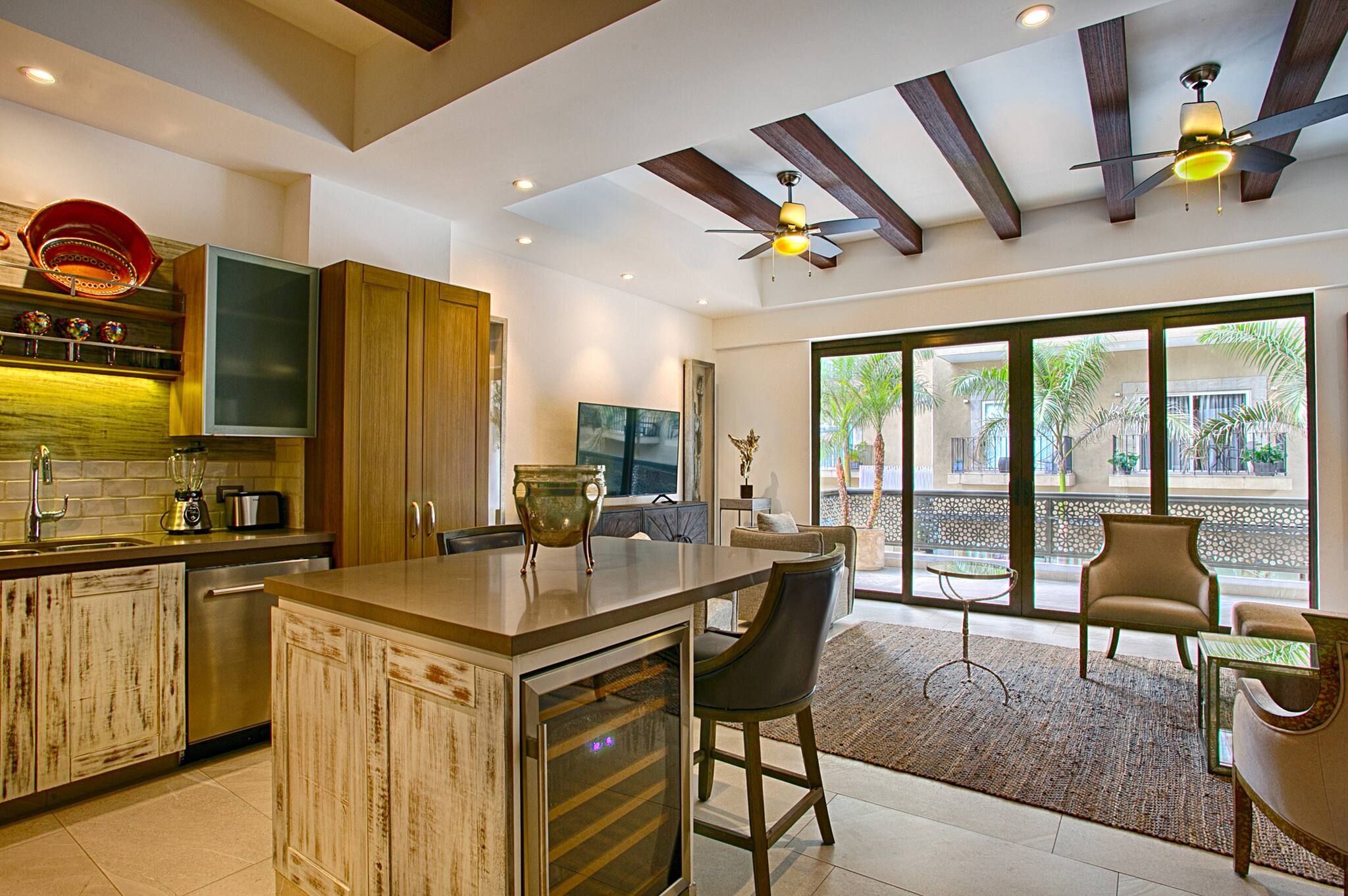 A modern kitchen with a bar area, wooden cabinets, and a large window overlooking a courtyard.